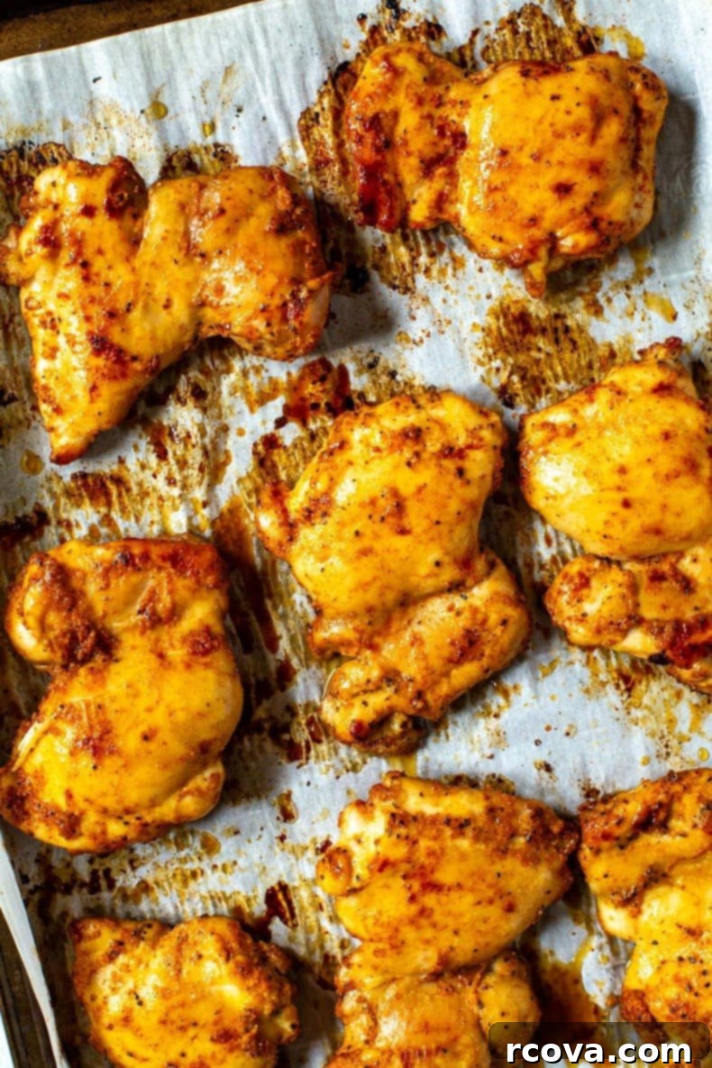 Juicy Baked Boneless Chicken Thighs 2 A close-up of seasoned baked chicken thighs on a sheet pan with prepared with parchment paper.