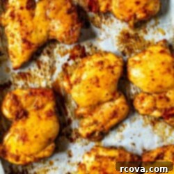 Juicy Baked Boneless Chicken Thighs 7 A close-up of seasoned baked chicken thighs on a sheet pan with prepared with parchment paper.