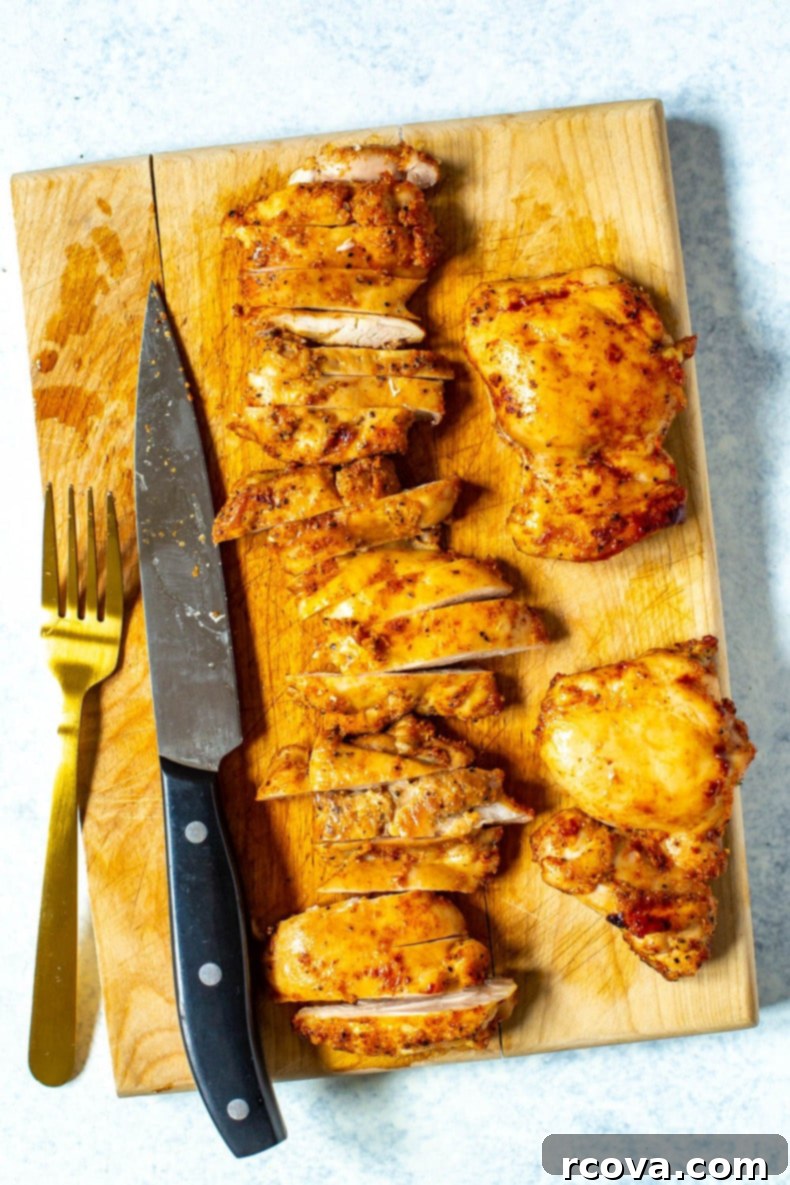 Juicy Baked Boneless Chicken Thighs 5 A cutting board pictured with a fork, knife, and chicken thighs being sliced.