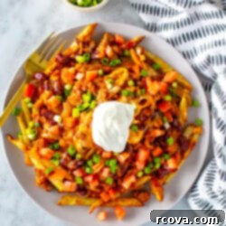 Next-Level Chili Cheese Fries 10 A big plate with chili cheese fries on top, loaded with tomato, green onions and sour cream.