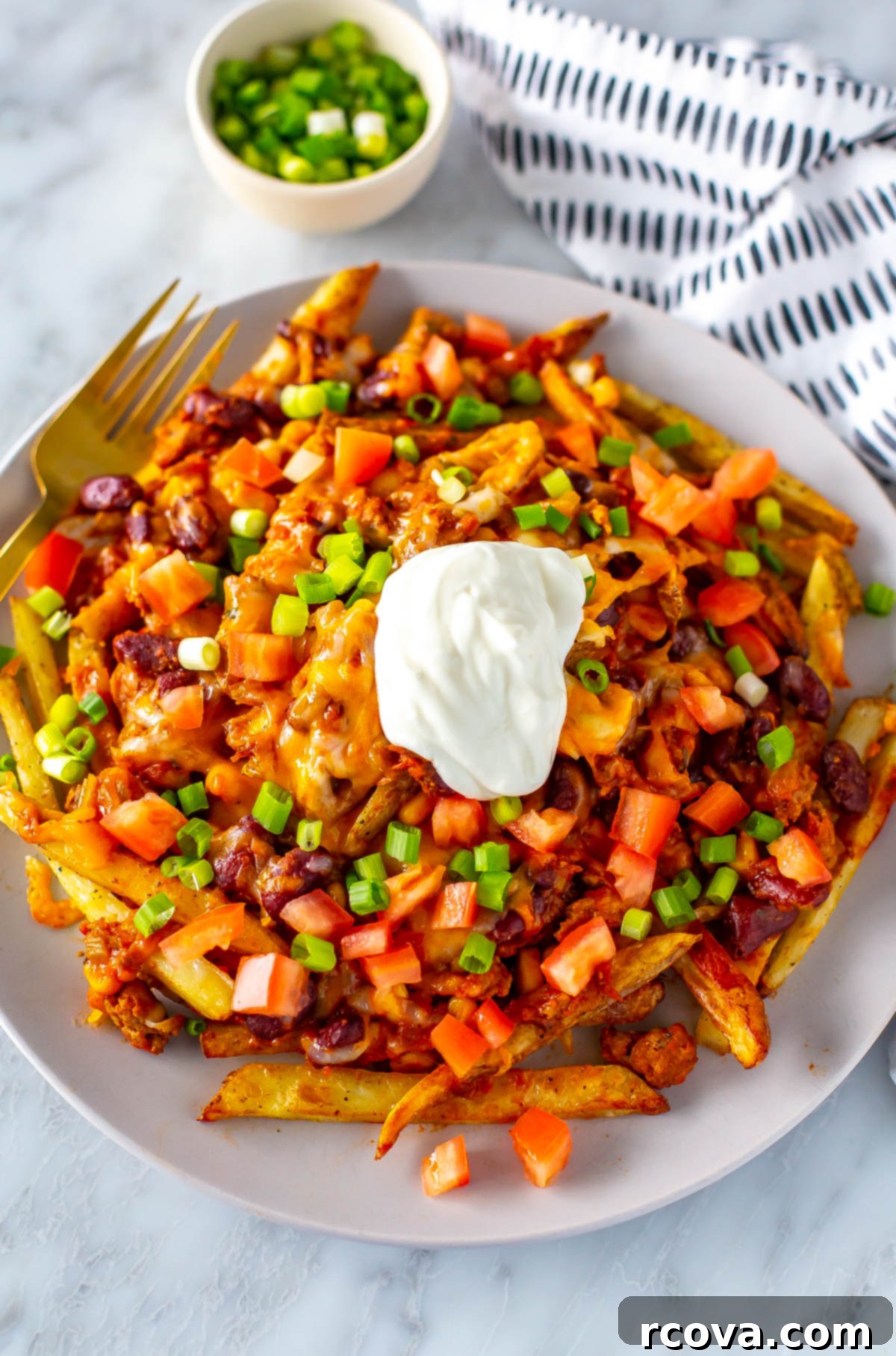 Next-Level Chili Cheese Fries 9 A big plate with chili cheese fries on top, loaded with tomato, green onions and sour cream.