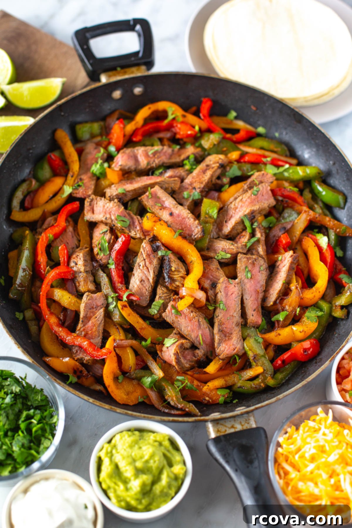 Sizzling Steak Fajitas 2 Overhead shot of vibrant steak fajitas in a cast iron skillet, featuring perfectly seared steak, colorful red and yellow bell peppers, and tender onions. Surrounding the skillet are bowls of fresh guacamole, tangy sour cream, shredded cheddar cheese, zesty salsa, and warm tortillas, inviting you to assemble your perfect fajita.