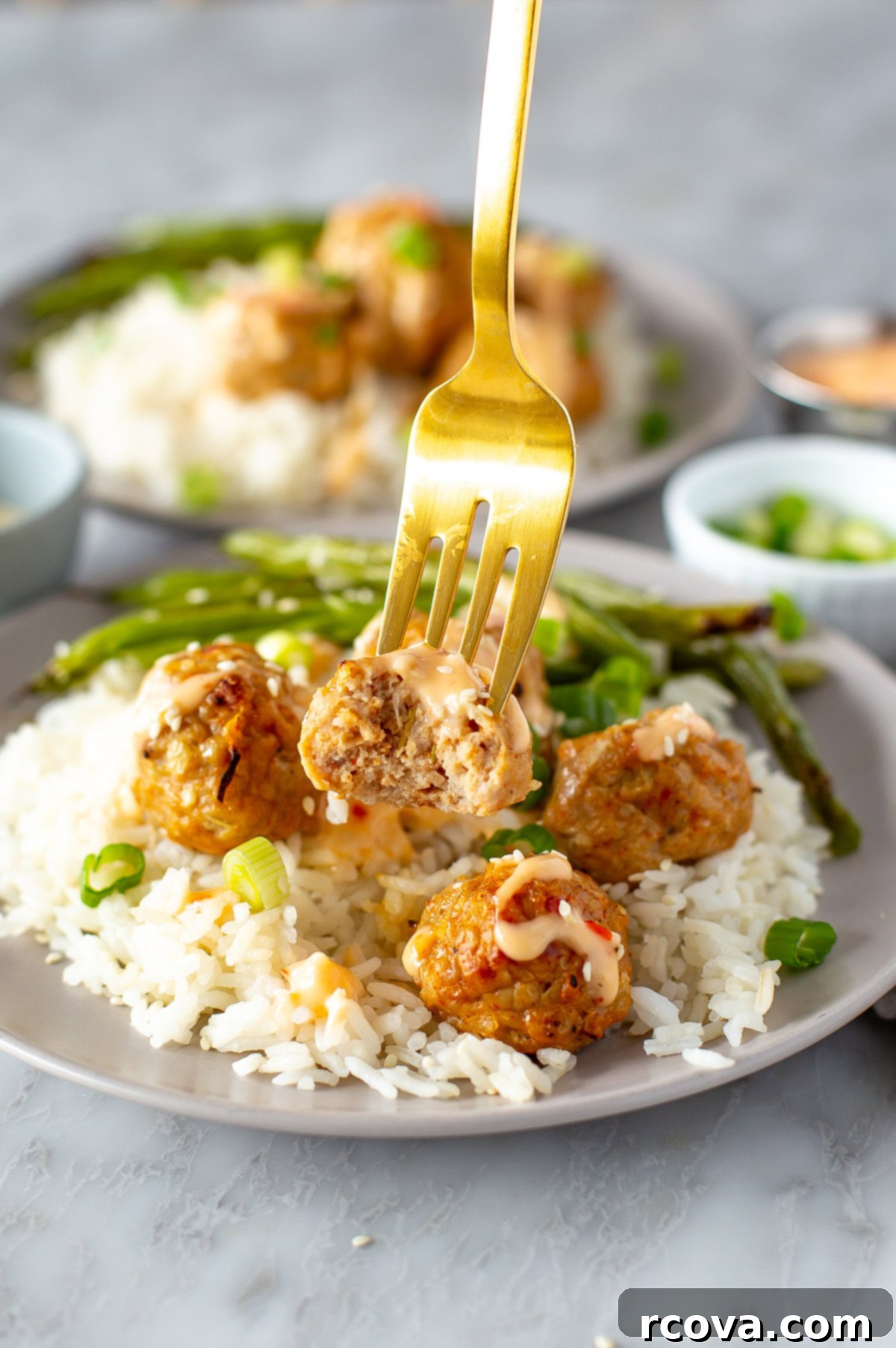 Sizzling Sweet Heat Meatballs 8 Firecracker meatball with a creamy sauce on a fork, over a serving of rice and green beans.