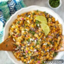 Fiesta Elote Pasta Salad 10 Overhead shot of Mexican street corn salad in a white bowl with lime wedges, cilantro, and crumbled feta cheese."