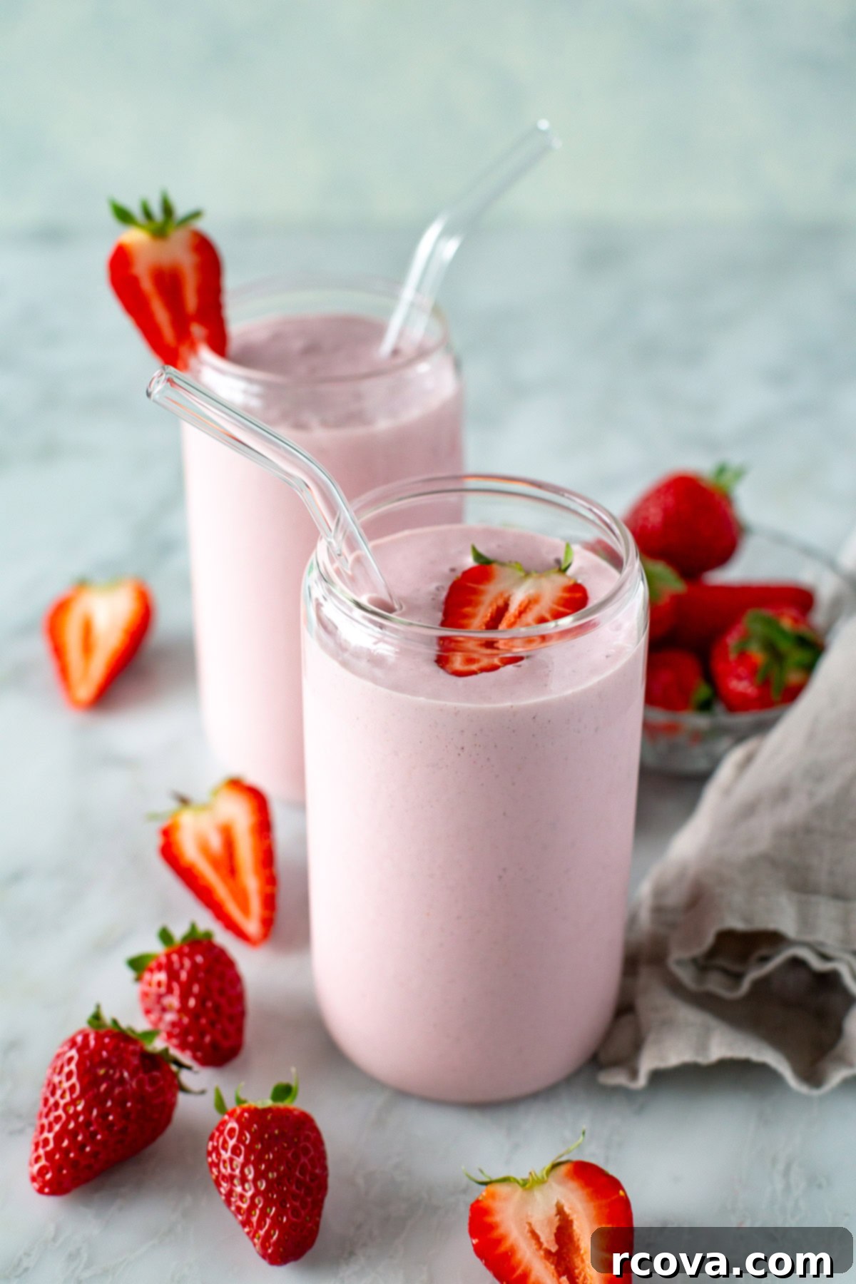 High-Protein Strawberry Power Smoothie 2 Two clear glasses filled with vibrant high-protein strawberry smoothie, surrounded by fresh strawberries, ready to be enjoyed.