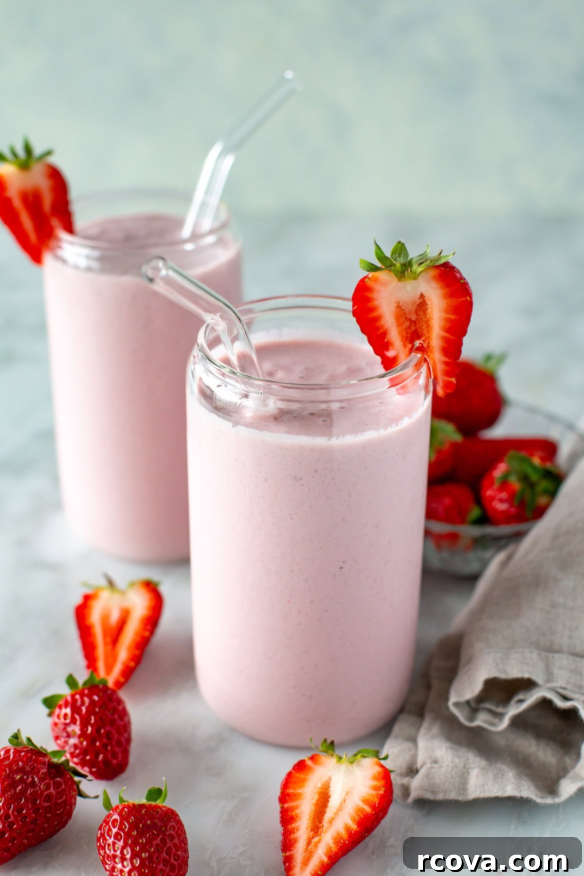 High-Protein Strawberry Power Smoothie 8 Side shot of two clear glasses filled with high-protein strawberry smoothie, garnished with strawberries, set on a rustic wooden surface.