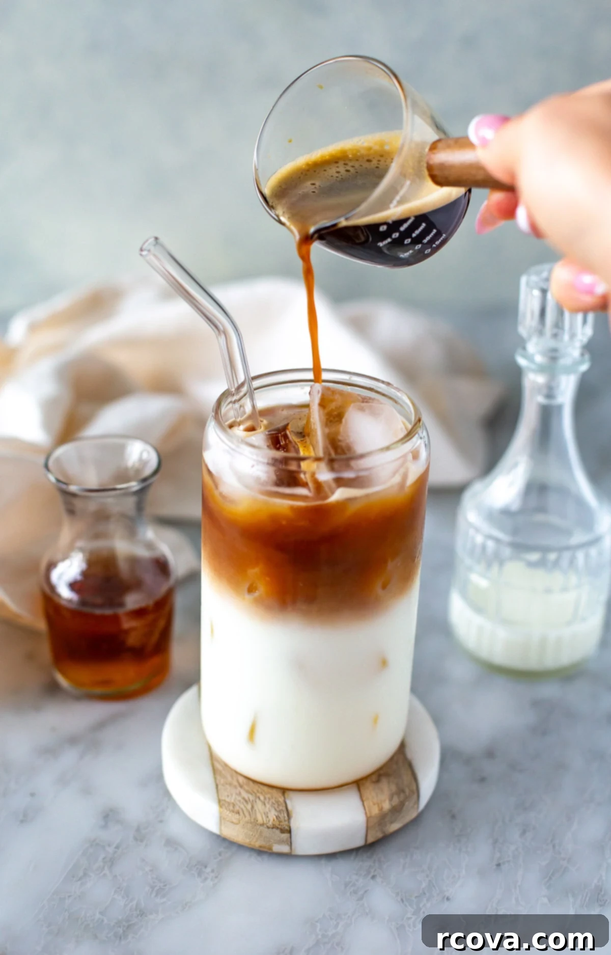 Instant Iced Vanilla Latte 9 Side shot of a hand pouring coffee into a glass with milk and ice for an iced vanilla latte.