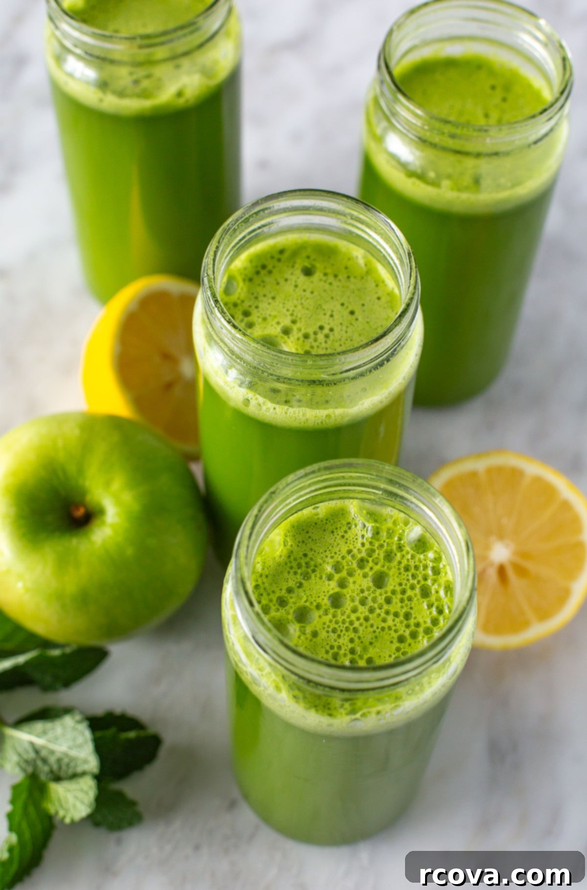 Your Quick Green Elixir 7 Overhead shot of four glasses of freshly made green juice, garnished with lemon slices and mint sprigs, highlighting its vibrant color and refreshing appeal.