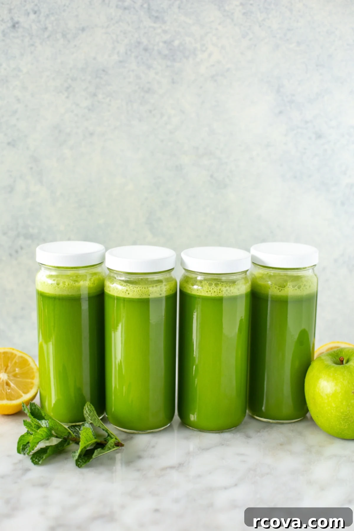 Your Quick Green Elixir 9 Side shot of four sealed glass jars filled with fresh green juice, neatly arranged alongside fresh fruit and mint, indicating readiness for healthy meal prep.
