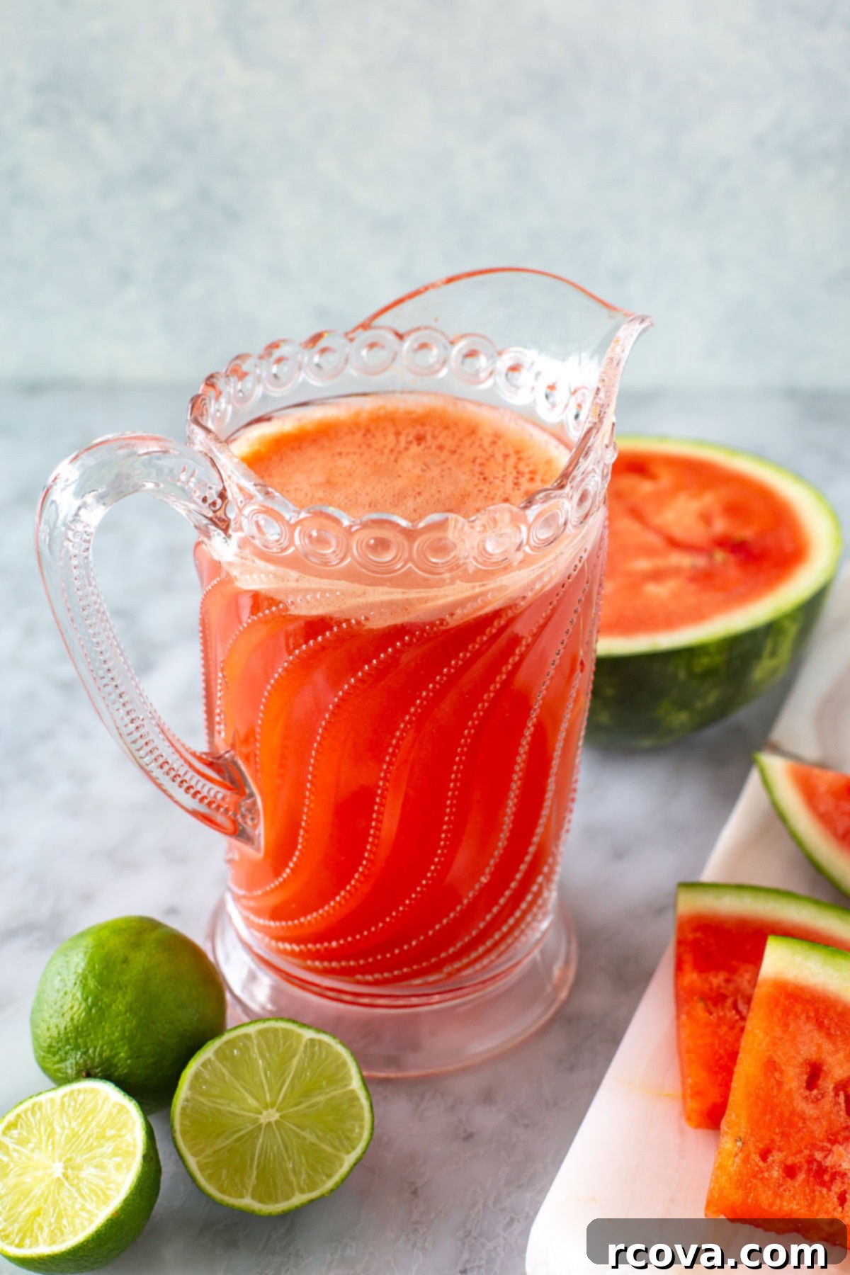 Ruby Red Watermelon Refresher 7 Side shot of a glass pitcher filled with watermelon juice and surrounding fresh fruit, ready to serve.