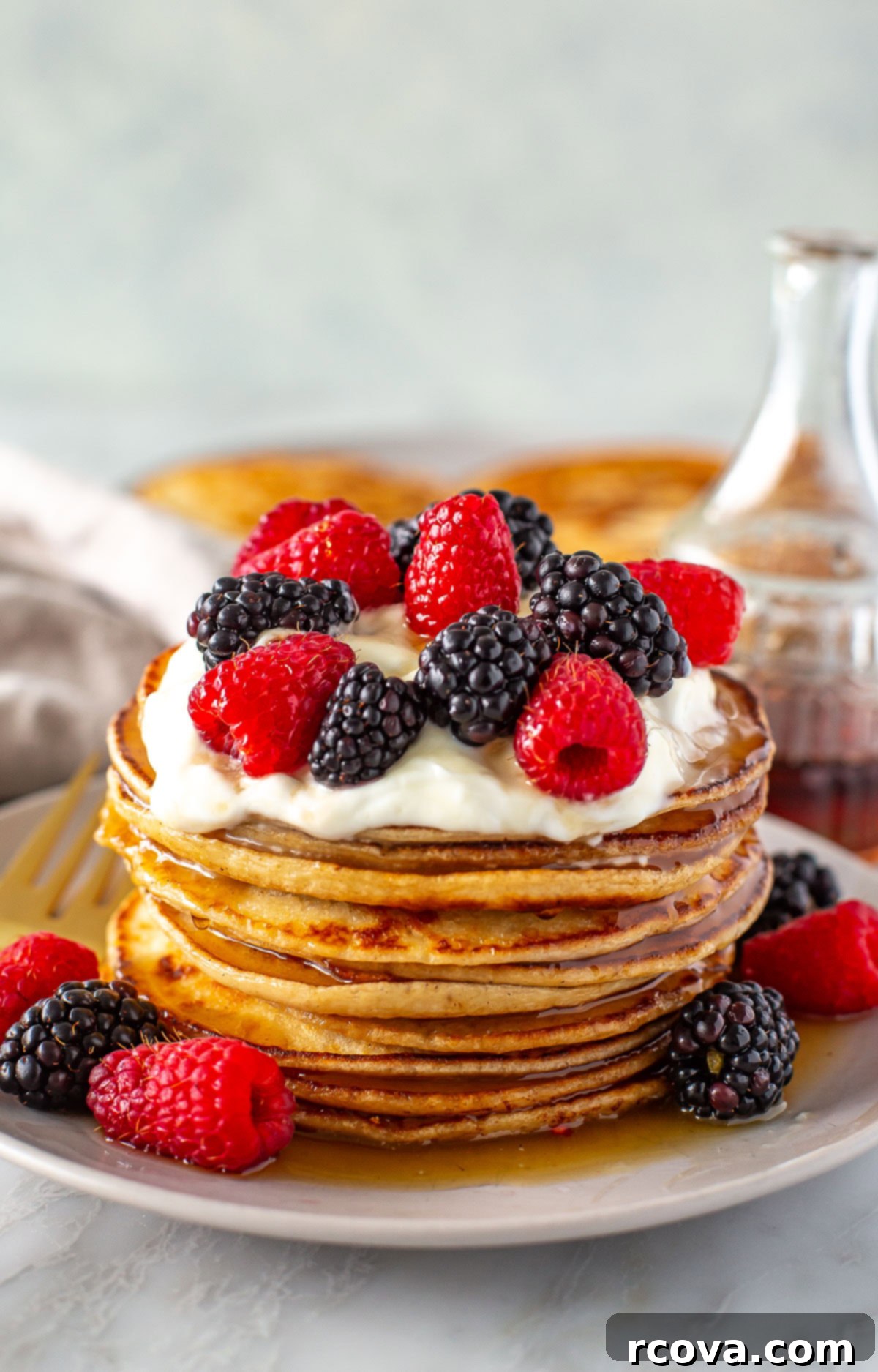 Protein-Packed Greek Yogurt Pancakes 2 Side shot of a tall stack of Greek yogurt pancakes with berries and cream.