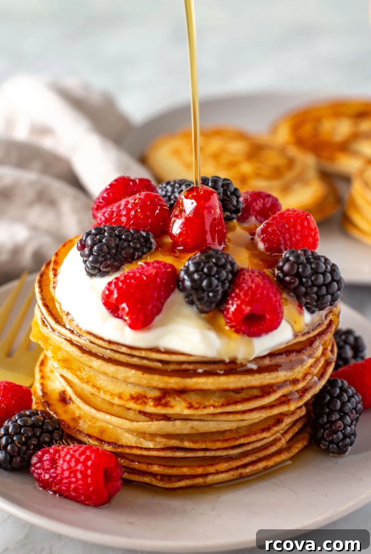 Protein-Packed Greek Yogurt Pancakes 8 Side shot of syrup being drizzled onto a stack of pancakes with berries.