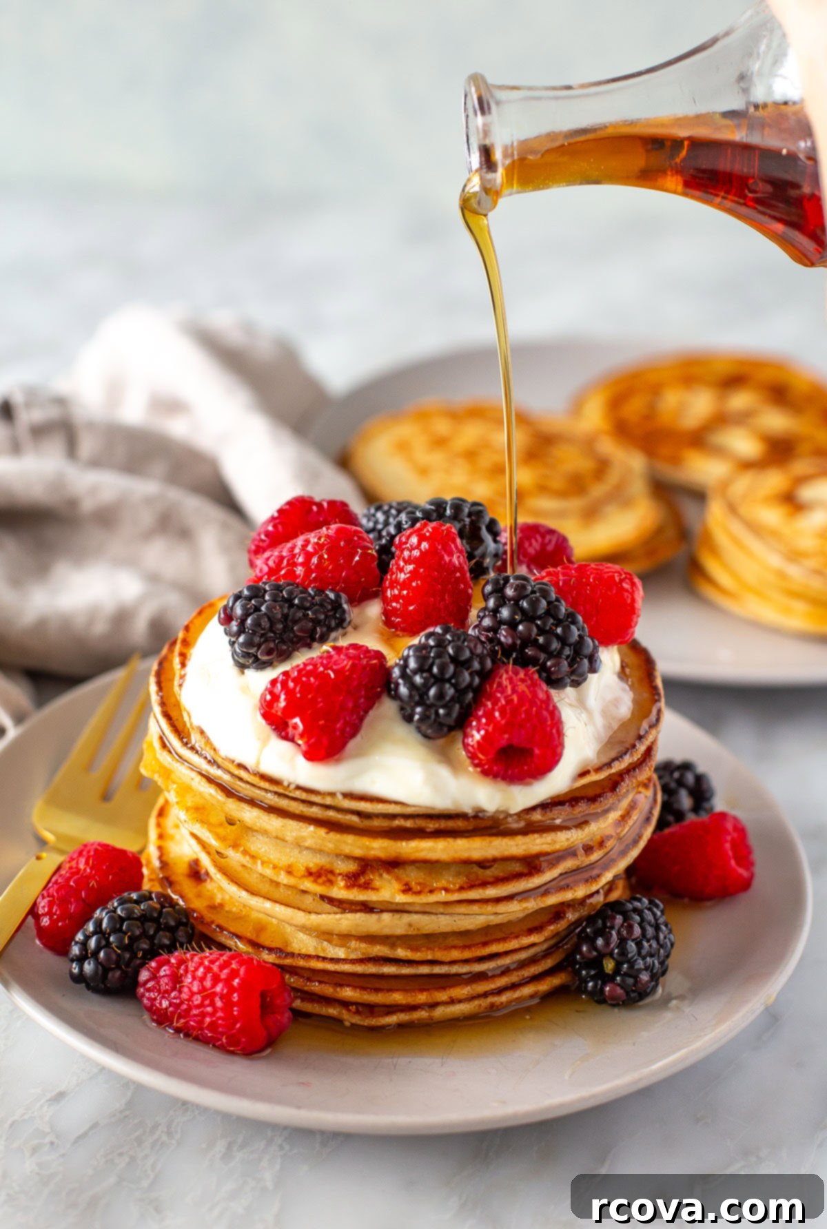 Protein-Packed Greek Yogurt Pancakes 9 Side shot of maple syrup being poured over a stack of pancakes with berries.