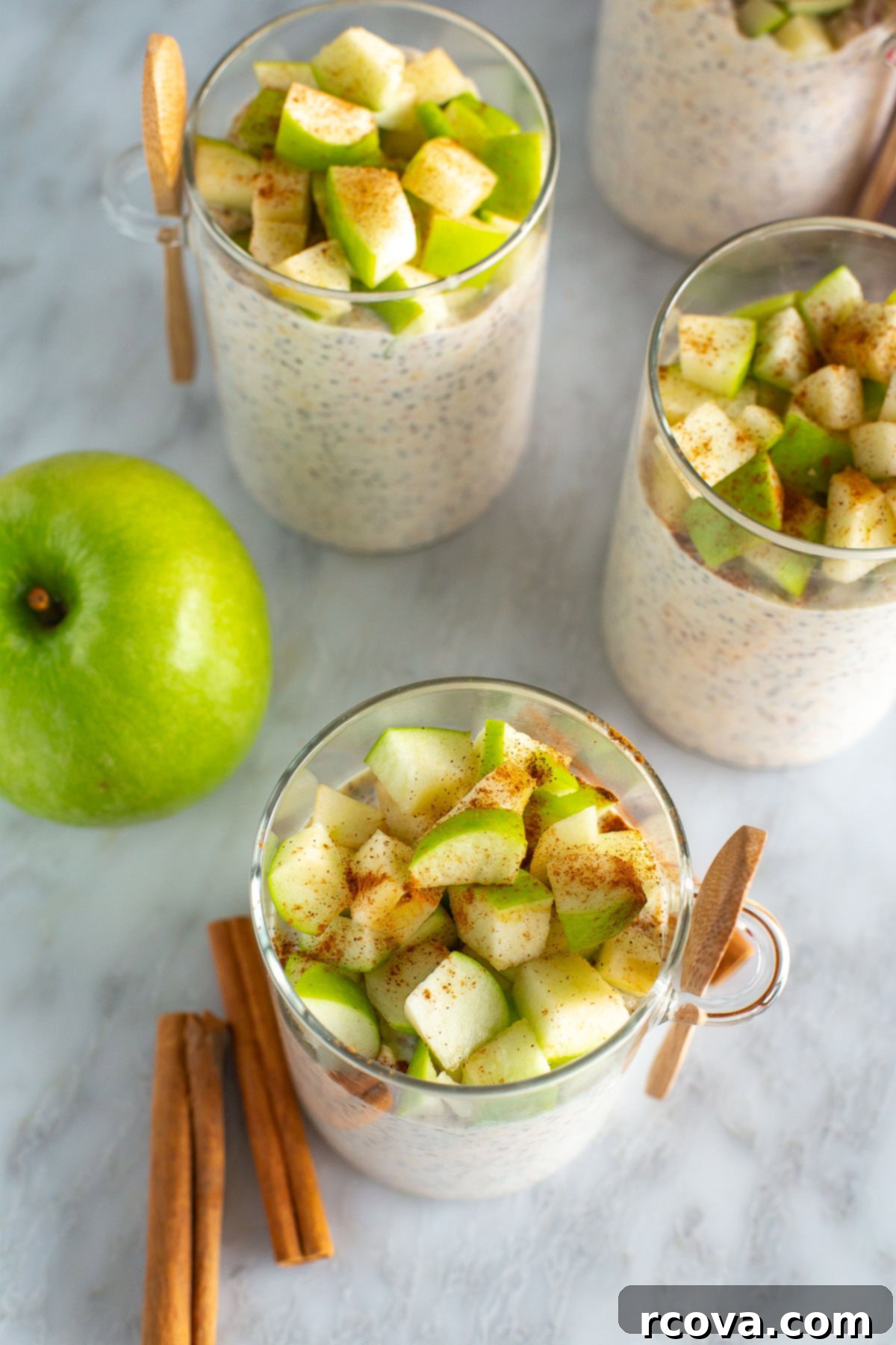 Cozy Apple Cinnamon Overnight Oats 6 An inviting overhead view of three jars of freshly made Apple Cinnamon Overnight Oats, beautifully presented on a kitchen counter alongside a fresh green apple and two aromatic cinnamon sticks.