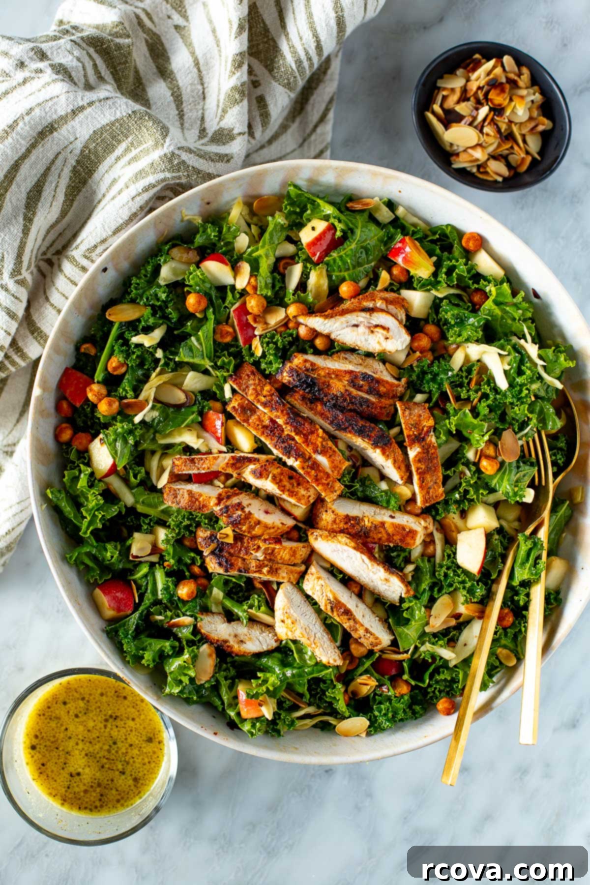 Ultimate Kale Crunch Salad 2 Overhead shot of a vibrant bowl of homemade kale crunch salad with chicken, a fork, and a side of creamy apple-dijon dressing.
