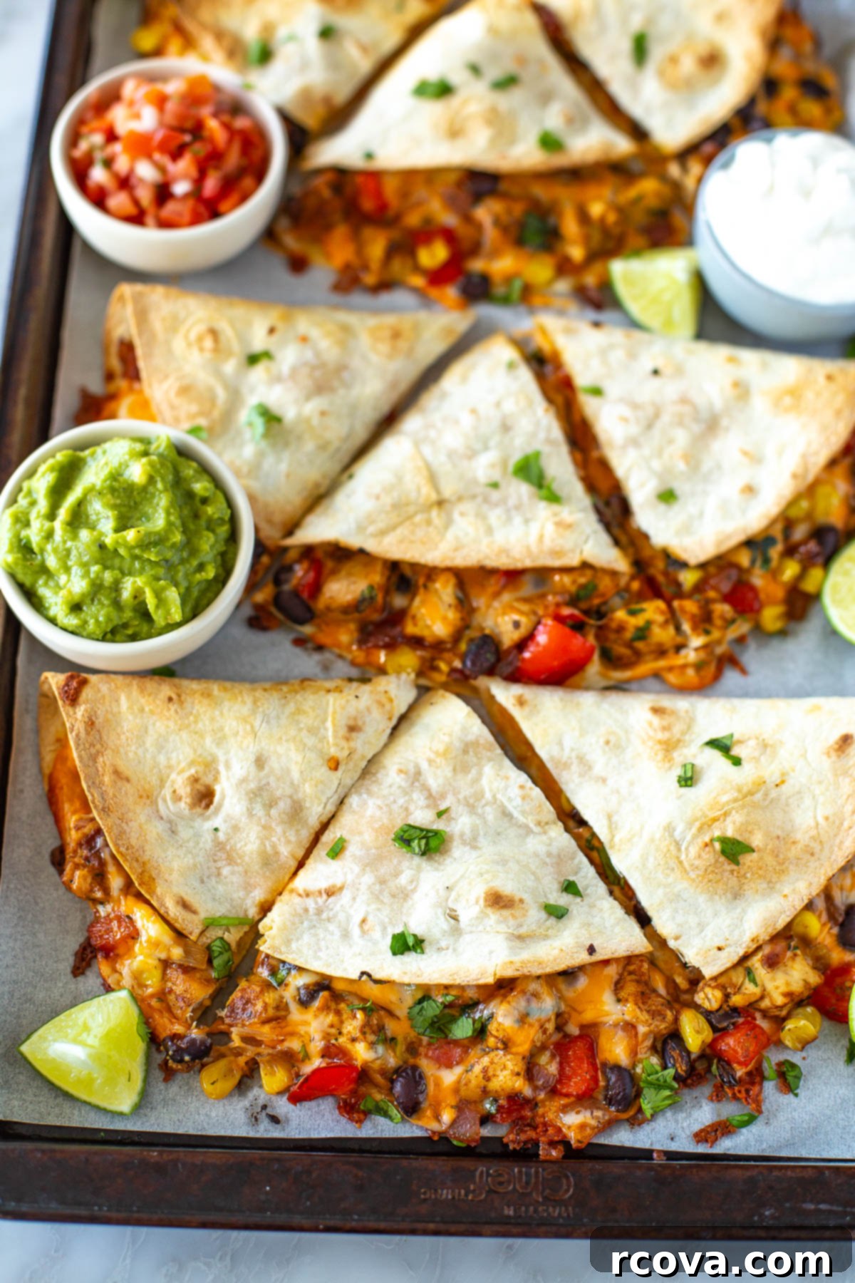 One-Pan Quesadilla Perfection 2 Overhead shot of a sheet pan full of finished quesadillas with side bowls of guacamole and salsa.