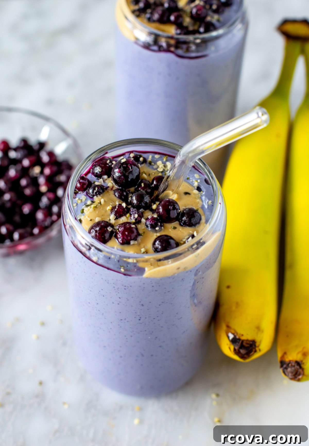 Blueberry Tofu Power Smoothie 6 Overhead shot of two purple tofu smoothies topped with blueberries and peanut butter, with bananas on the side.