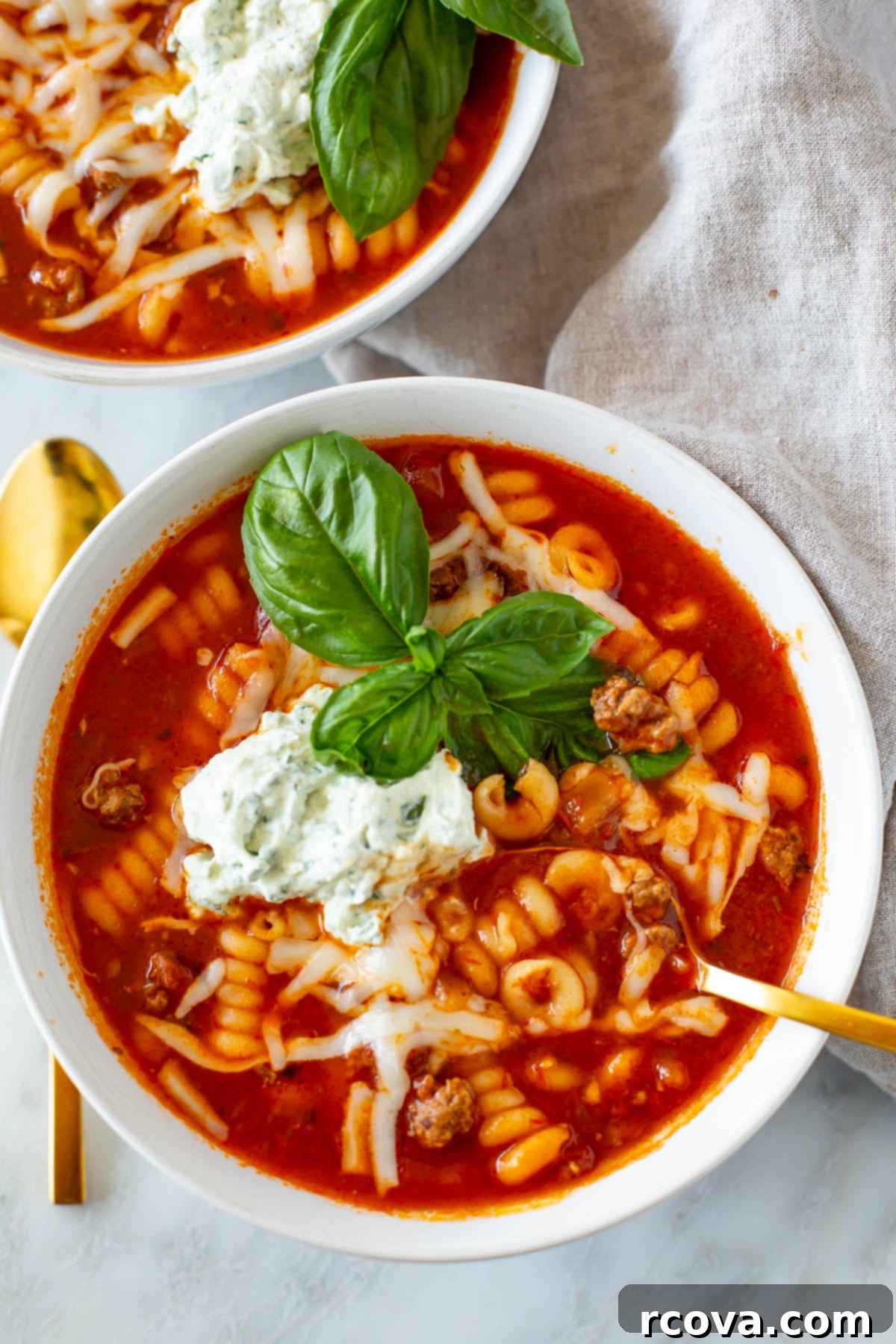 Effortless Slow Cooker Lasagna Soup 2 Overhead shot of a bowl of Easy Crockpot Lasagna Soup with a gold spoon, garnished with fresh basil.
