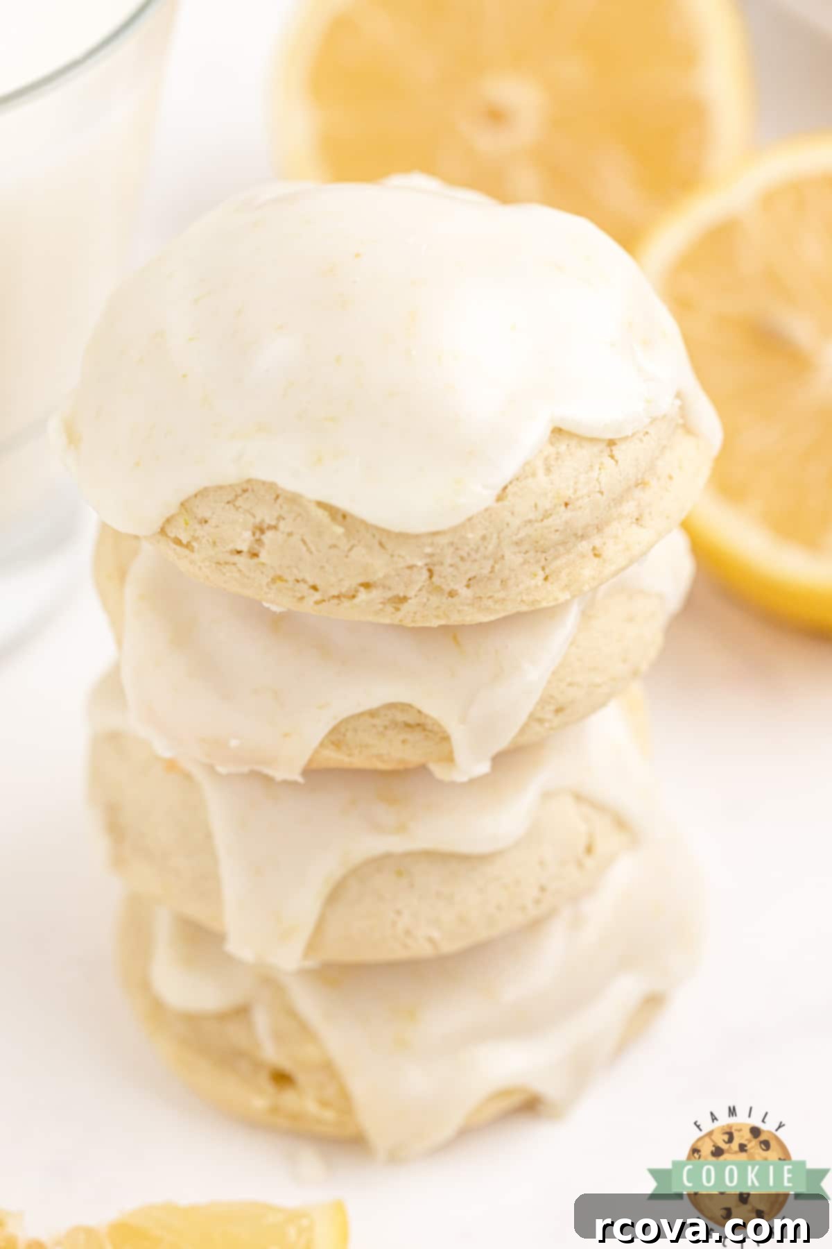 Sunshine Lemon Cheesecake Cookies 8 A close-up of a stack of freshly baked Lemon Cream Cheese Cookies with a bright yellow glaze, garnished with lemon zest, on a rustic surface.
