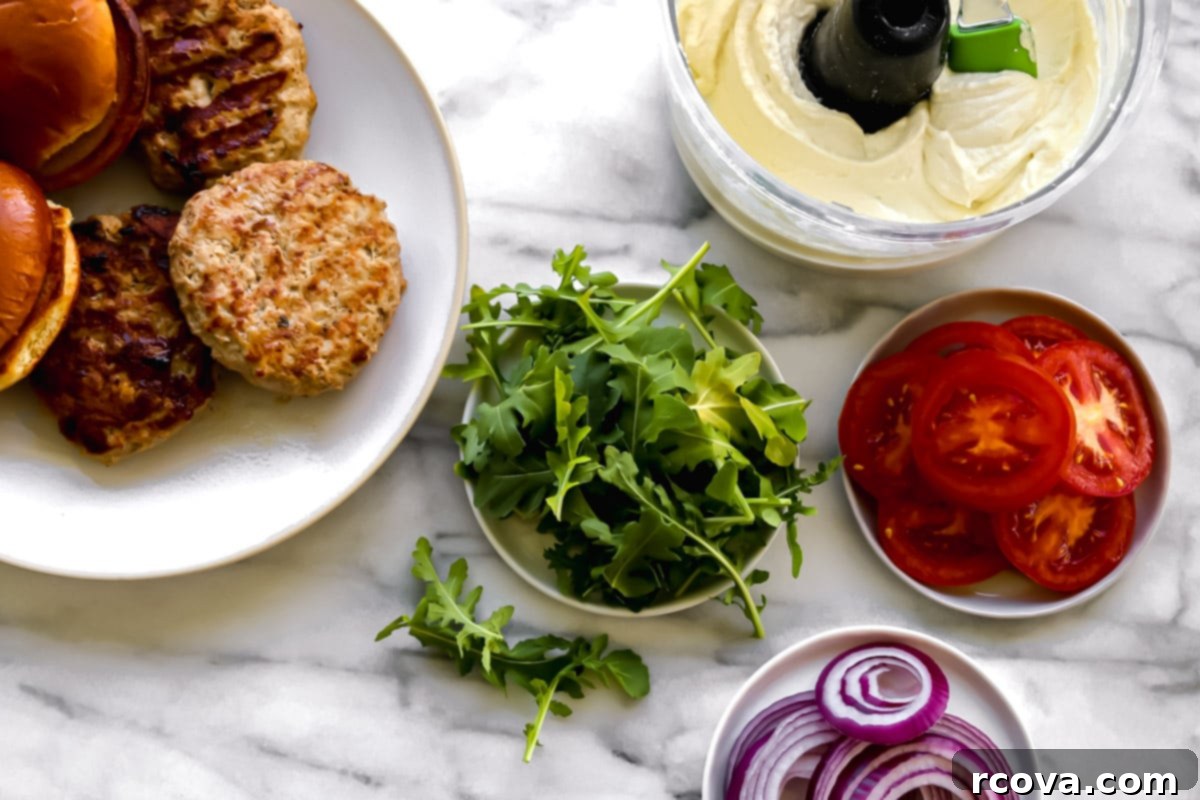 Silken Feta Turkey Burgers 4 Ingredients for assembling the turkey burgers: cooked turkey patties, brioche buns, fresh arugula, sliced tomatoes, and red onion, alongside a bowl of creamy whipped feta spread.