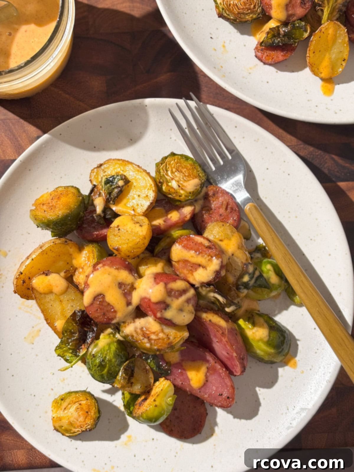 Sheet Pan Chicken Sausage and Veggies 5 A serving of roasted chicken sausage and vegetables on a white plate, garnished with fresh herbs.